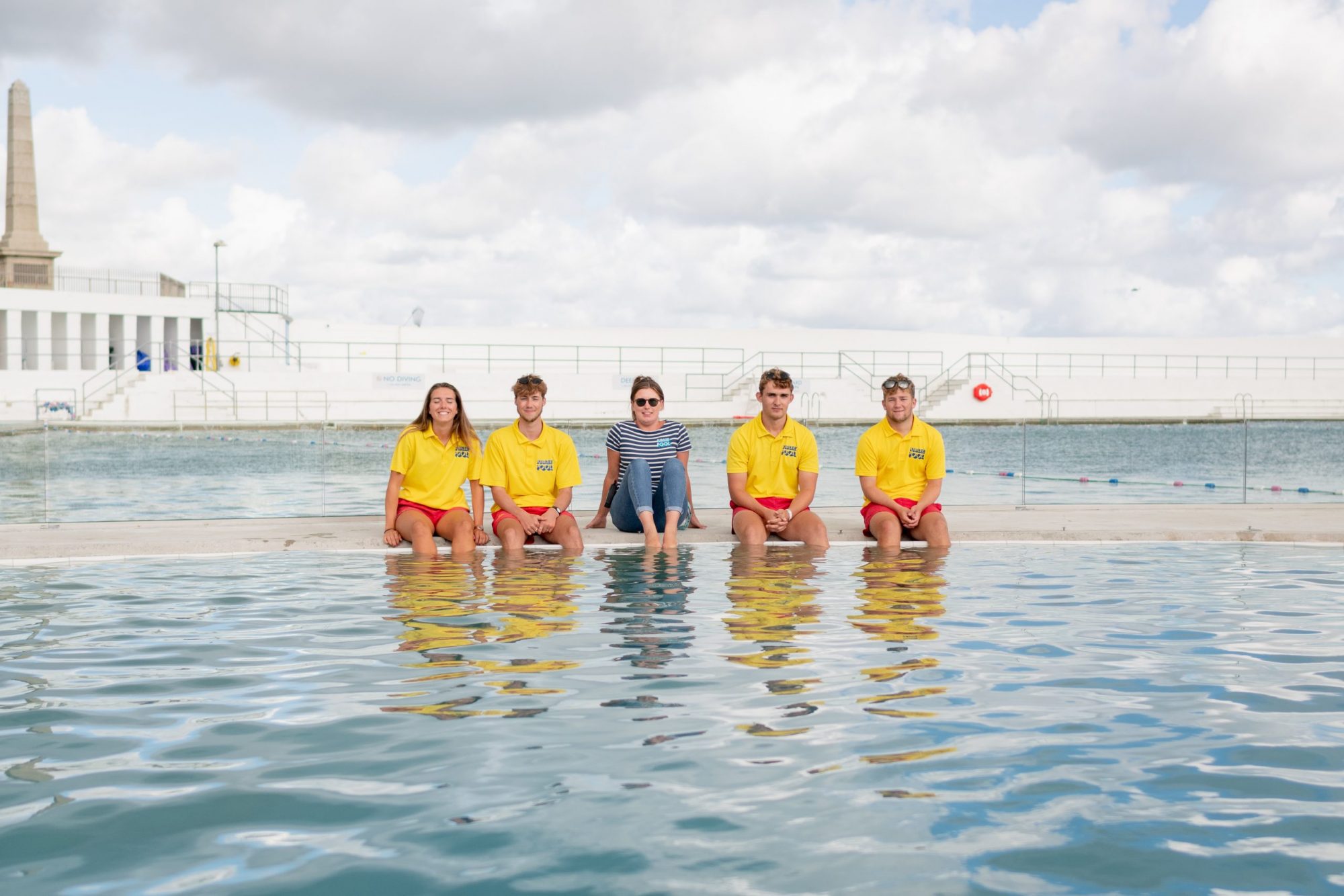 four lifeguards and a member of staff sitting on the edge of the pool