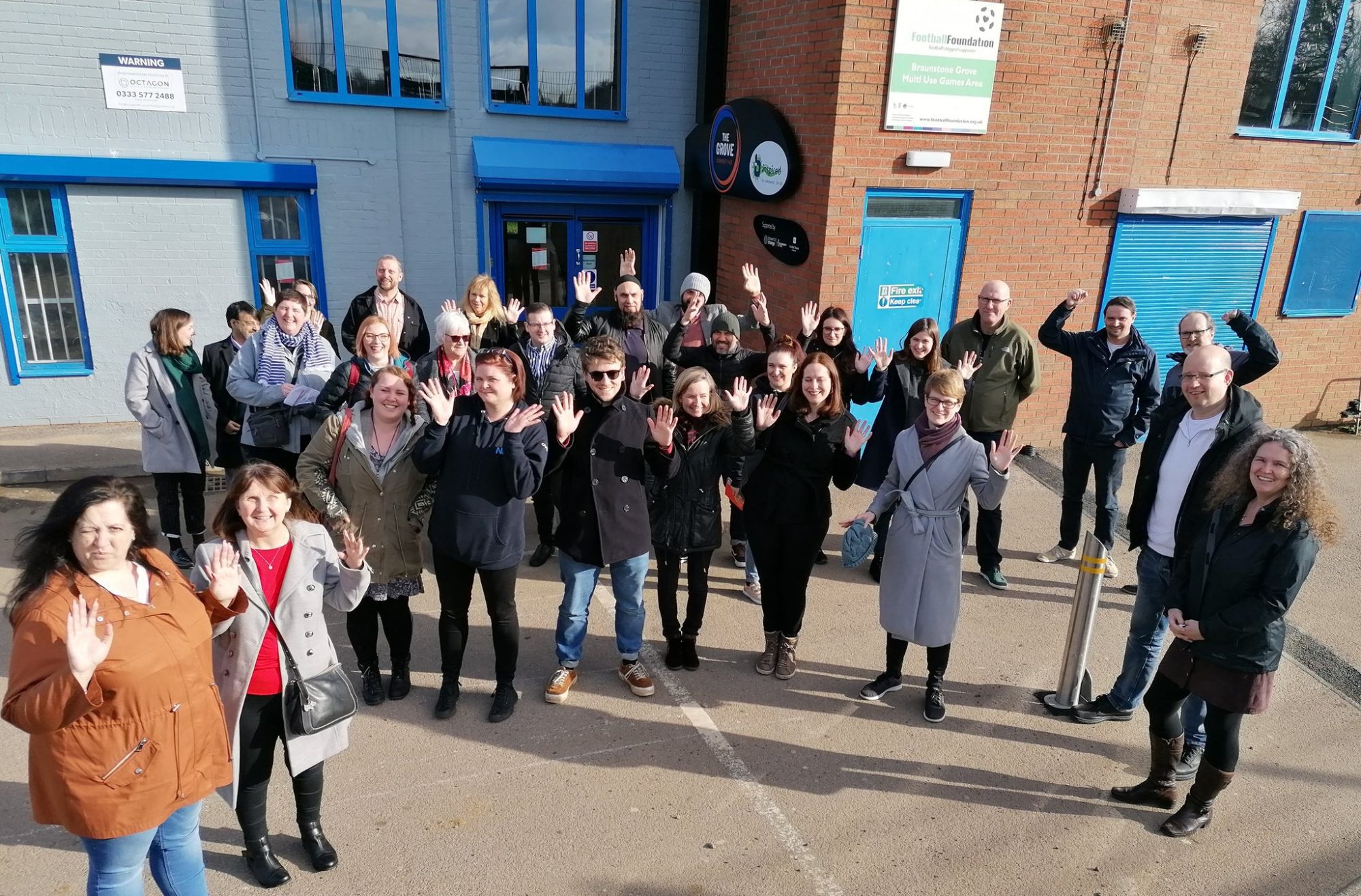 Participants of the Empowering Places Learning Camp in Leicester raising their hands in front of a building