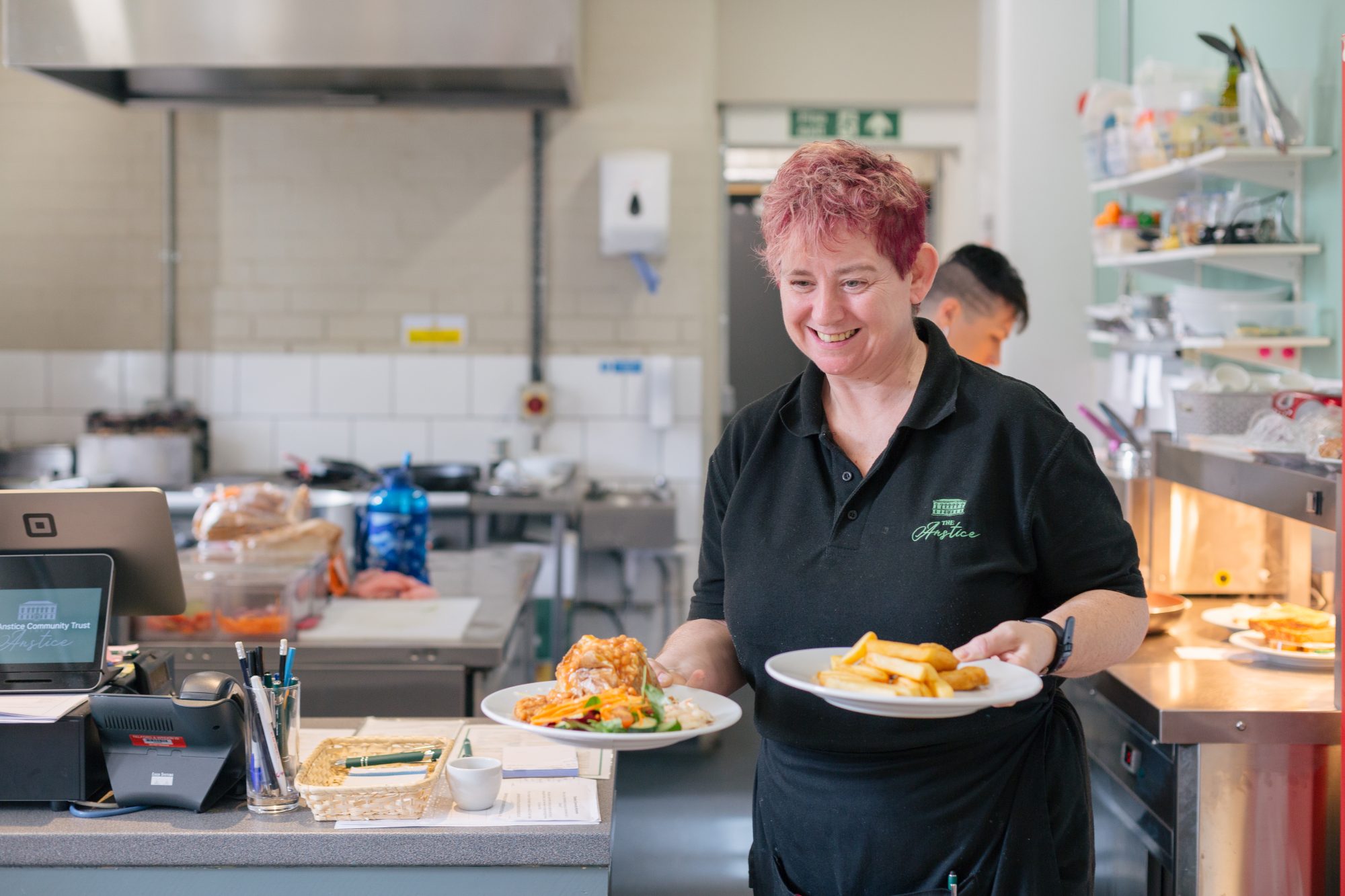 Waiter with pink hair carries plates of food from the kitchen at the Anstice's cafe.