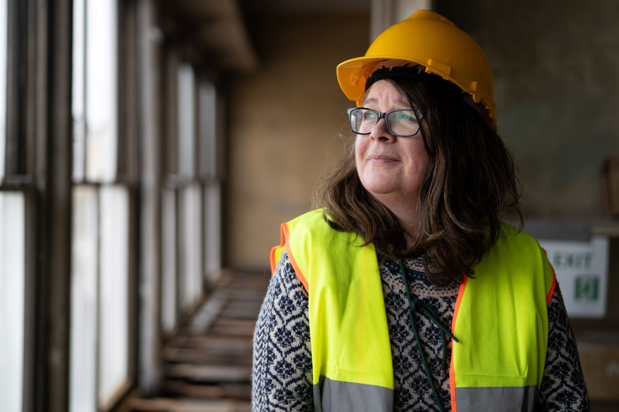 Sharon George, Shademakers UK, looking out of a window. She's wearing high vis and a hard hat.