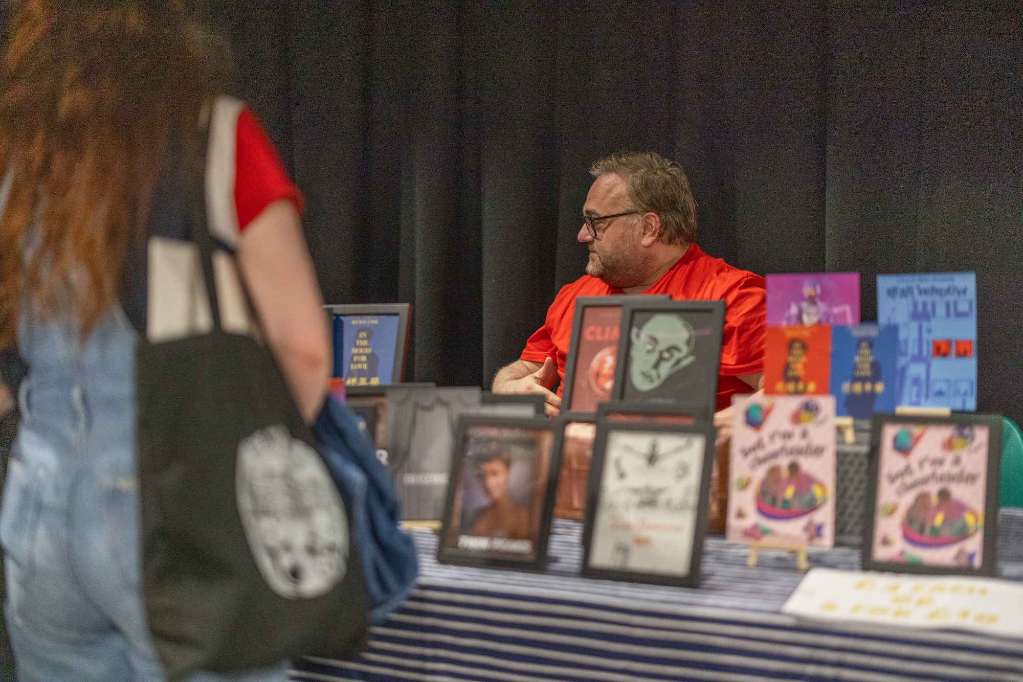 man in a red tshirt sat behind a stall